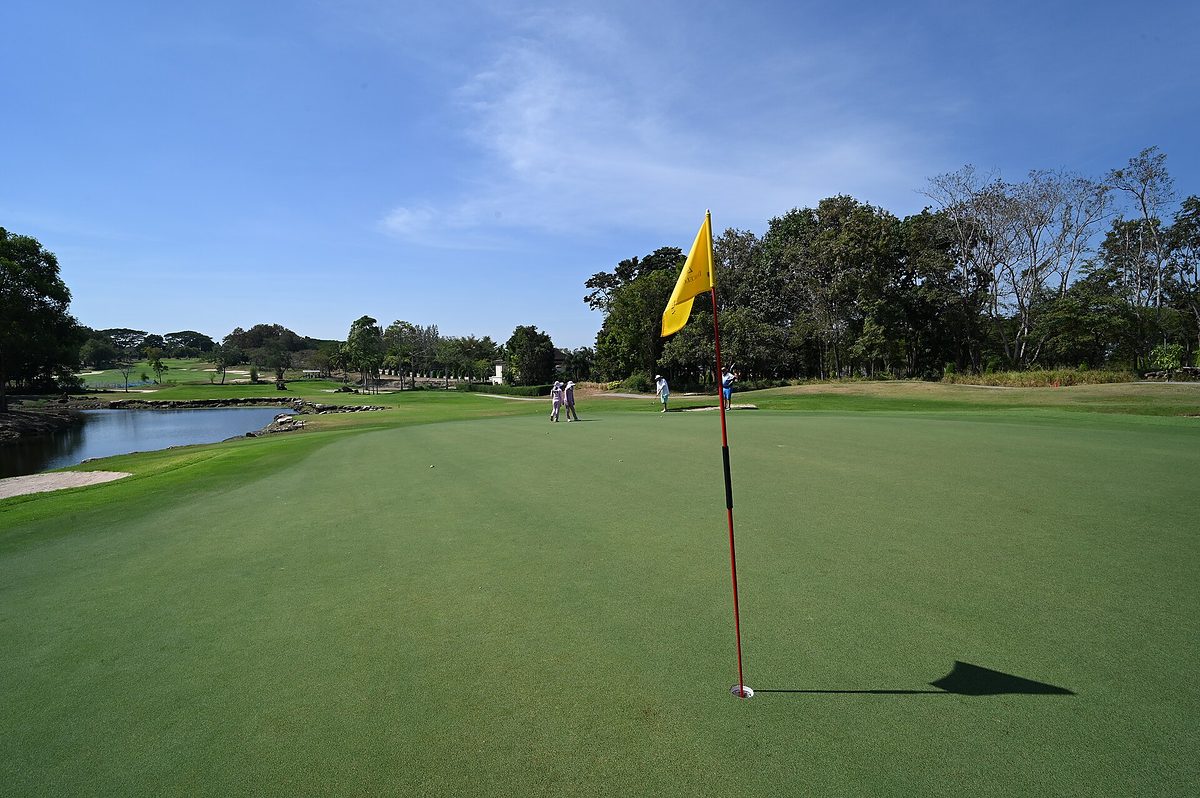 Un green de golf avec son drapeau jaune, au bord d'un étang